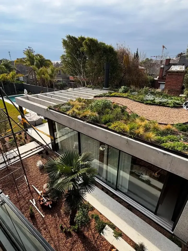 Techo verde sobre una galería, plantado con gramíneas y senderos de grava, y una palmera en el patio de abajo